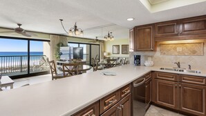 A spacious kitchen with wooden cabinets, a large island, and a view of the ocean through the sliding glass doors.
