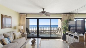 A modern living room with a sofa, coffee table, TV, and a balcony with a view of the ocean.