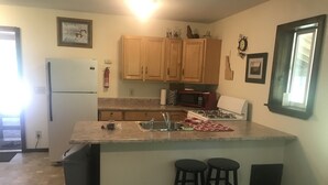 Una cocina con armarios de madera, un refrigerador, un microondas, un lavamanos y dos taburetes.