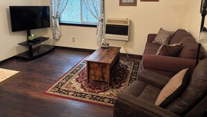 Una sala de estar con un televisor de pantalla plana, una mesa de centro de madera, un sofá marrón, un tapete estampado y cuadros enmarcados en la pared.