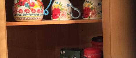 Un meuble de cuisine contenant divers objets, notamment un pichet à motifs floraux, des tasses, des bols et un récipient rempli de portions individuelles de yaourt.