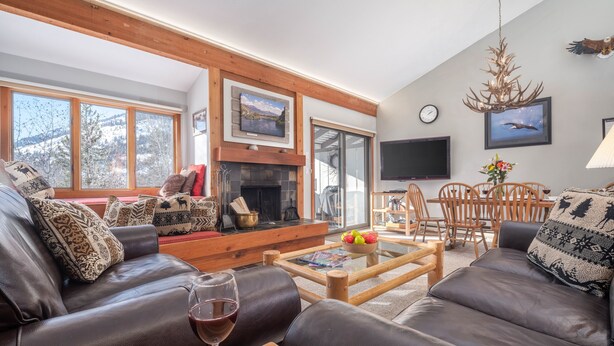 Un salon chaleureux avec des canapés en cuir, une cheminée, un coin repas et de grandes fenêtres donnant sur l’extérieur.