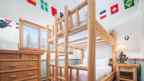 Une chambre avec un lit superposé, une commode, une table de chevet, une lampe et des drapeaux accrochés au mur.