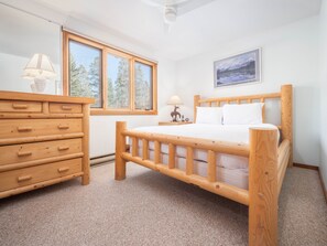 Relax in a serene bedroom with a comfortable bed and a dresser, offering a peaceful view of the surrounding trees.