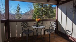 Un espace extérieur aménagé, abrité, avec deux chaises en métal et une petite table ronde, agrémenté d’un vase avec des fleurs et de deux verres à vin.