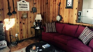 A cozy room with a red sofa, a round coffee table, a lamp, and a sign reading "Historical Landmark 715 Nolden St Los Angeles". - The High Country Hobo Preserve: Rustic Cabin (Descanso)
