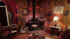 A cozy room with a fireplace, wooden walls, a couch, a table, and Christmas decorations. - The High Country Hobo Preserve: Rustic Cabin (Descanso)