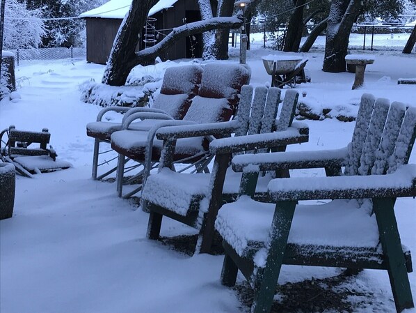 Outdoor wooden chairs covered in snow, a wooden bench, and a metal table in a snowy park setting.