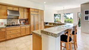 Uma cozinha moderna com bancadas de granito, armários de madeira e uma ilha grande com banquetas.