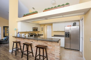A kitchen with a central island, bar stools, a refrigerator, and a microwave. - Beautiful Pool Home Close To Many Beaches (Venice)