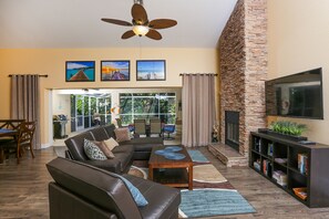 A spacious living room with a leather sofa, a coffee table, and a fireplace. There is a television mounted on the wall and a bookshelf filled with books. - Beautiful Pool Home Close To Many Beaches  (Venice)
