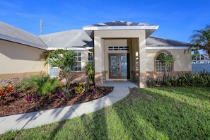 A modern house with a front entrance, a covered porch, and a landscaped garden with various plants. - Beautiful Pool Home Close To Many Beaches (Venice)