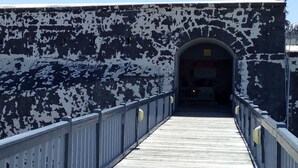 A wooden pedestrian bridge with a metal railing and a white and black wall on one side.