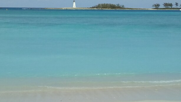 A beach with clear turquoise water, a white lighthouse, and a sandy shore.