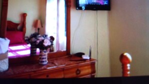 A bedroom with a wooden bed, a dresser, and a television mounted on the wall.