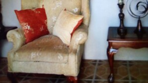 A vintage armchair with a red pillow and a small wooden table beside it.