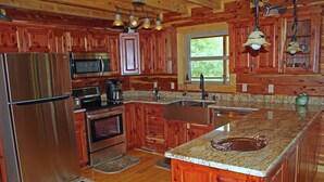 A kitchen with wooden cabinets, stainless steel appliances, granite countertops, and a window providing natural light. - Trumpeter Lodge located on the banks of Little Red River, Heber Springs,Arkansas (Heber Springs)