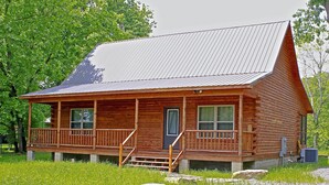 A log cabin with a porch, a front door, and a metal roof. - Trumpeter Lodge located on the banks of Little Red River, Heber Springs,Arkansas (Heber Springs)