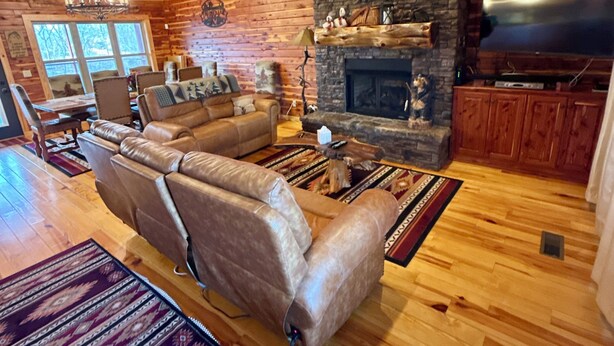 A spacious living room with a large leather sofa, a stone fireplace, and a ceiling fan. - Trumpeter Lodge located on the banks of Little Red River, Heber Springs,Arkansas (Heber Springs)