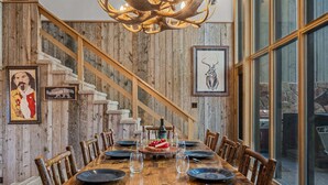 Un espace repas comprenant une table en bois, des chaises, un lustre et un escalier.