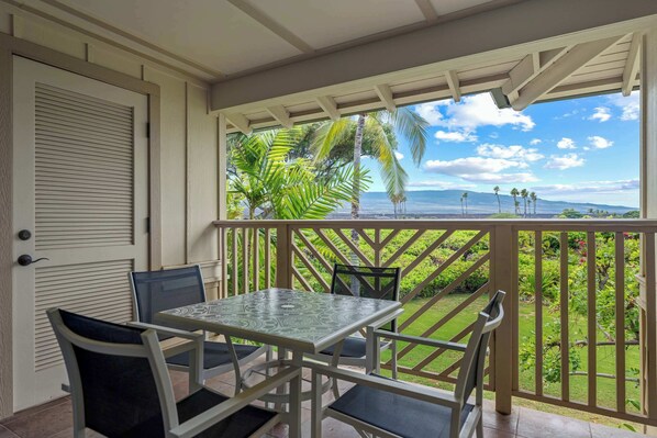 A balcony with a table and chairs, overlooking a lush garden and a scenic view of the ocean.