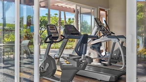 Un espace dédié à la remise en forme, équipé de tapis de course et d’appareils elliptiques, avec de grandes fenêtres donnant sur un paysage verdoyant et un bâtiment situé à l’extérieur.