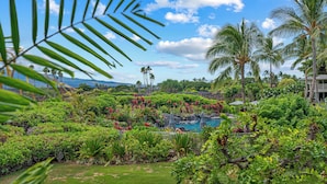Un jardin luxuriant avec une piscine, des palmiers et une vue sur l’océan.