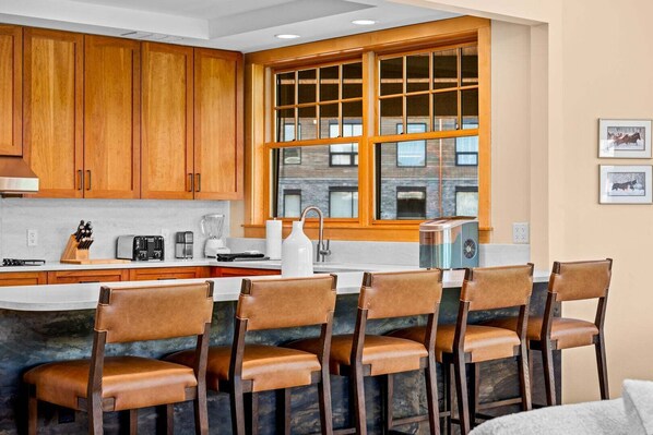 A kitchen with wooden cabinets, a large window, and a bar area with stools.