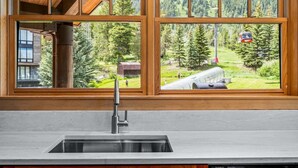 A kitchen with a stainless steel sink and wooden window frames overlooking a mountainous landscape. - RMR: Cody House B Condo in Teton Village (Teton Village)