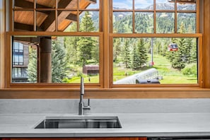 A kitchen with a stainless steel sink and wooden window frames overlooking a mountainous landscape.