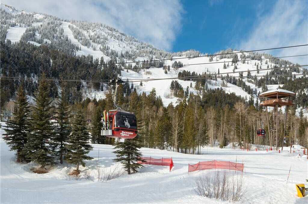 A ski lift in a snowy mountainous area with trees and a clear sky.