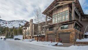 A modern two-story building with large windows and a stone facade, surrounded by snow and trees. - RMR: Cody House B Condo in Teton Village (Teton Village)