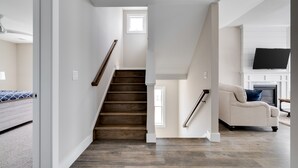 Una escalera conduce a un segundo piso con techo plano y un televisor montado en la pared.