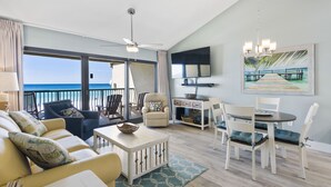 Un vaste salon avec un balcon donnant sur l’océan, un coin repas et un téléviseur fixé au mur.