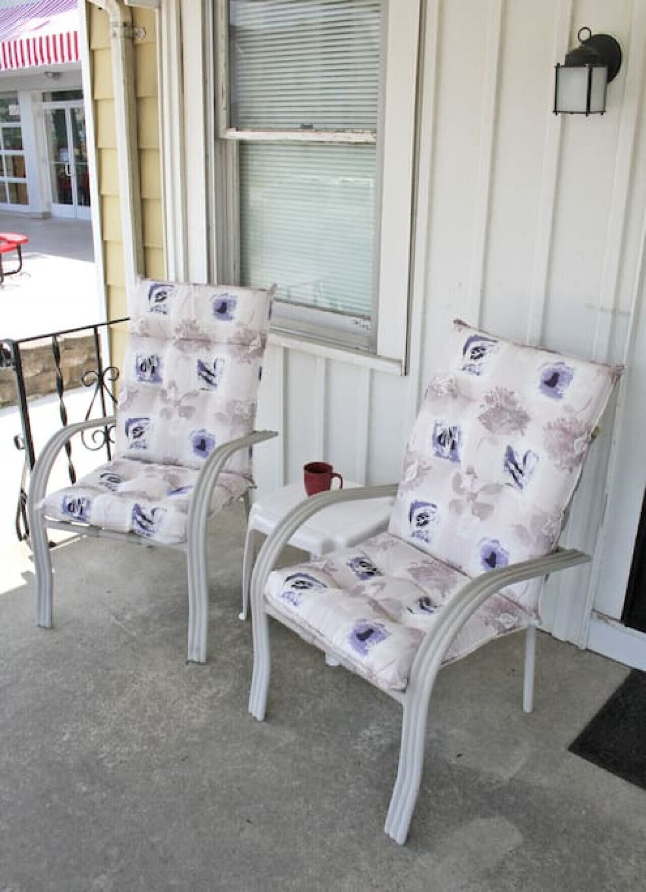 Two white chairs with floral upholstery on a porch with a metal railing.