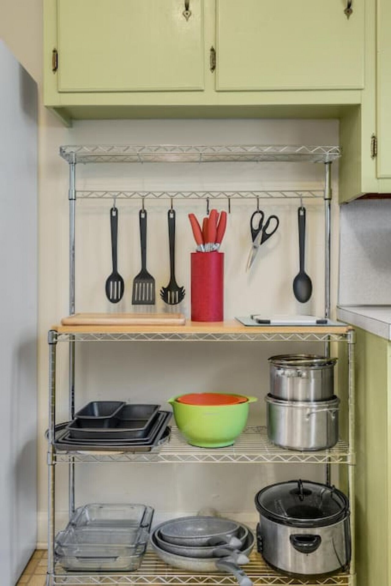 A kitchen with a metal shelf unit holding various utensils, cookware, and a red container.