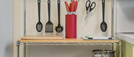 A kitchen with a metal shelf unit holding various utensils, cookware, and a red container.