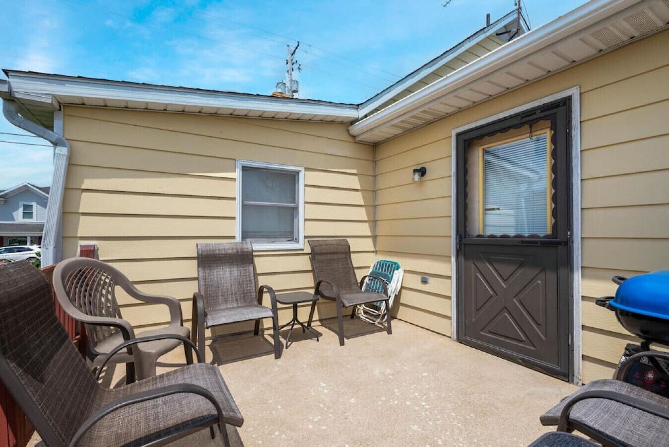A covered patio area with four chairs and a small table, a black door, and a blue grill.