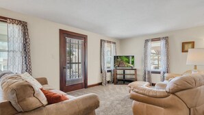 Un salon avec deux canapés beige, un téléviseur posé sur un meuble et une porte avec une fenêtre.