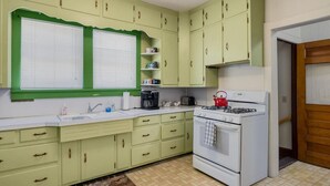 Une cuisine avec des meubles de couleur verte, une cuisinière blanche et une fenêtre avec des stores.