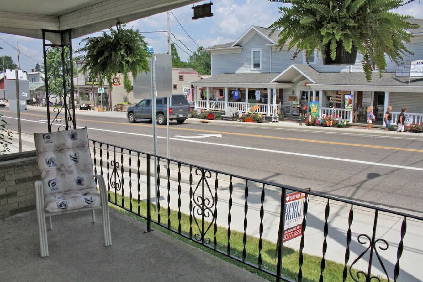 A roadside view with a chair, a 'SLEEP HERE' sign, and a house with a porch.