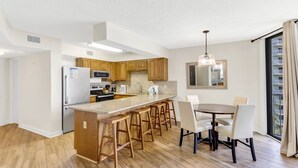 Une cuisine moderne avec des meubles en bois, un îlot central doté de tabourets de bar, une table à manger et une grande fenêtre offrant une belle vue.