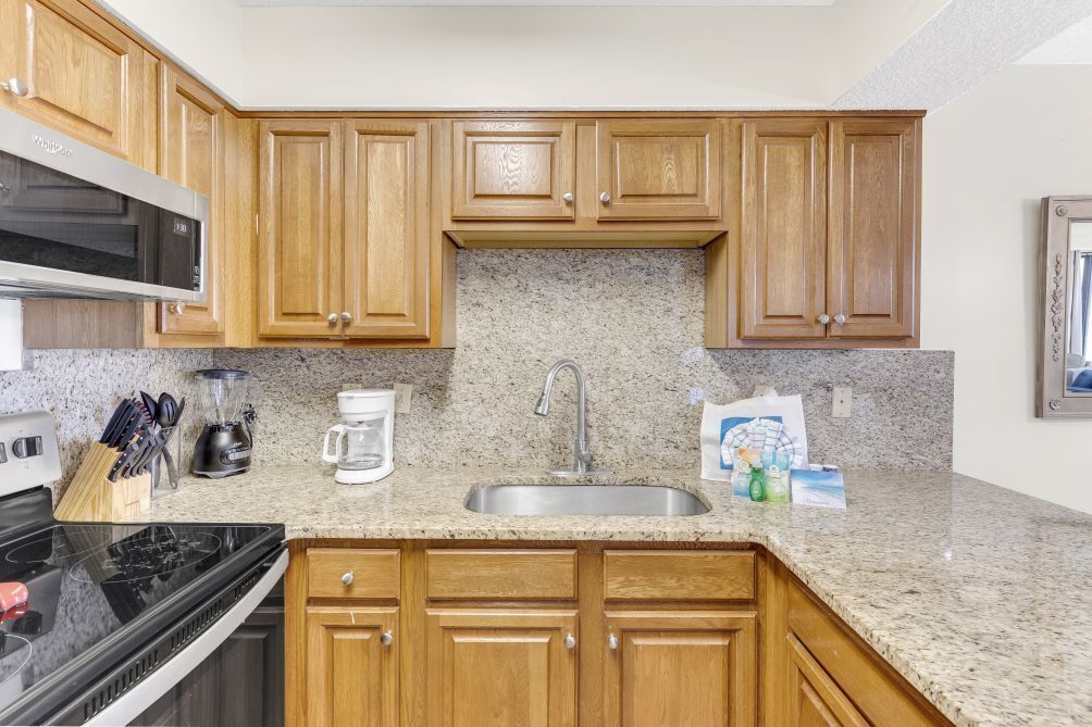 A kitchen with wooden cabinets, a granite countertop, a stainless steel sink, a microwave, a stove, and various kitchen appliances.