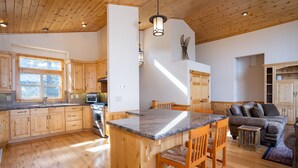Eine geräumige Küche mit Holzsäulen, einer zentralen Kochinsel mit Barhocker und einem Essbereich mit Sofa und Stühlen.