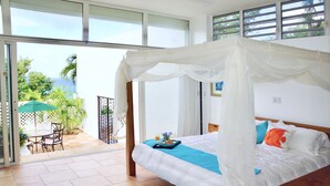 A bedroom with a bed, a nightstand, a window, and a view of the outdoors.