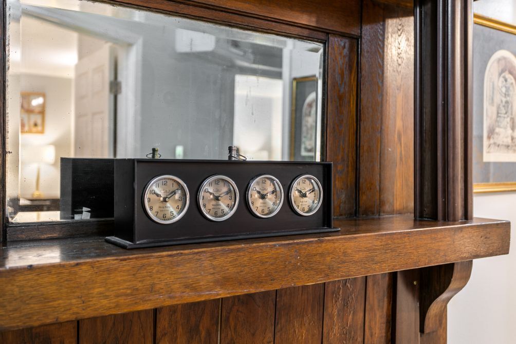 A wooden shelf with a black clock displaying four faces, each showing different times.