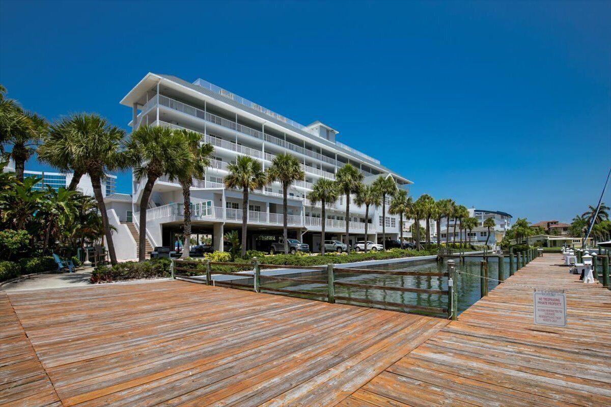 A modern hotel with multiple balconies, a wooden boardwalk, and palm trees.