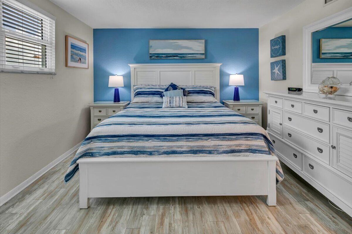 Un dormitorio con cama, mesitas de noche, cómoda y ventana con persianas.