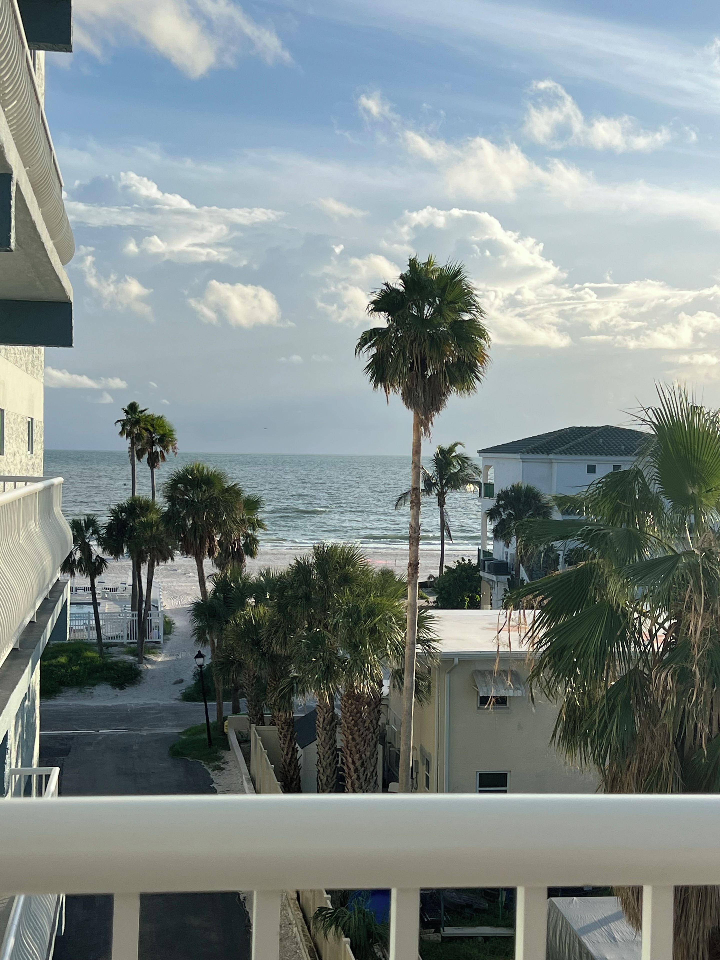 A balcony overlooking a beach with palm trees and a view of the ocean.