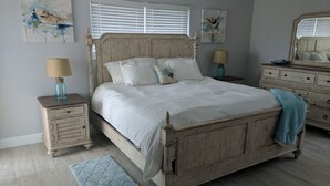A bedroom with a wooden bed, two bedside tables, a dresser, and a window with blinds. - Beautiful San Remo on Beach, Water-view From All Windows, Heated Pool, Hot Tub  (Redington Shores)